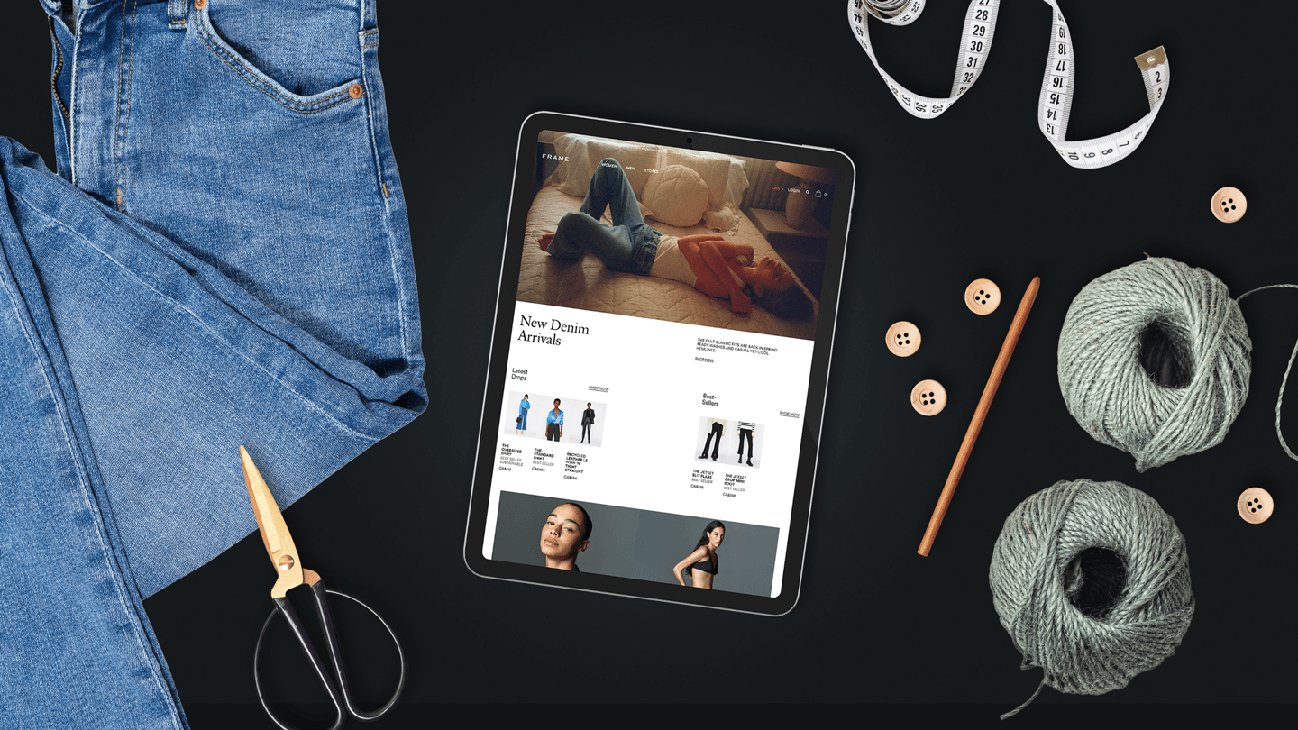 Flatlay of the Frame denim website on an iPad surrounded by a pair of jeans, threads, measuring tape, buttons, and a pair of scissors.